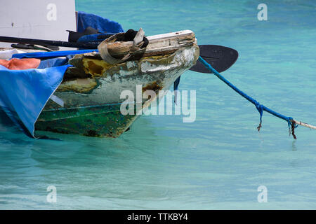 old fishing boat filled with junk moored by frayed rope in turquoise ocean water Stock Photo
