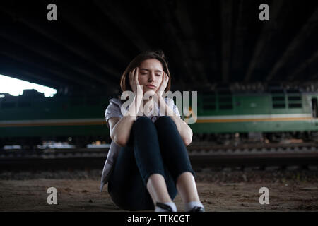 Sad woman sitting on the ground near the trains Stock Photo