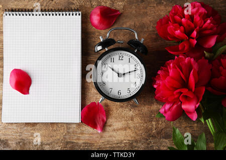 Vintage clock, peony flowers and notebook on wooden background Stock Photo