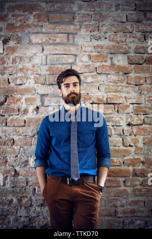 Portrait of confident businessman standing against brick wall in office Stock Photo