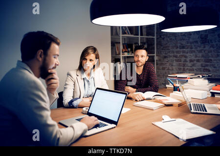 Colleagues looking at businessman using laptop in conference room Stock Photo