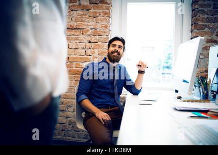 businessman looking at colleague while sitting at desk in office Stock Photo
