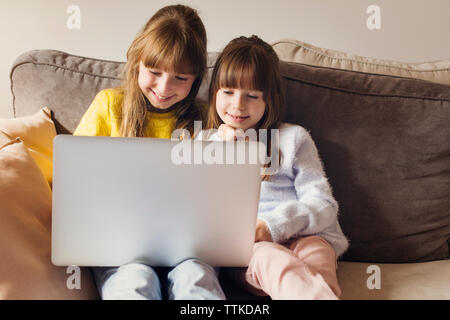 Sisters using laptop while sitting on sofa at home Stock Photo