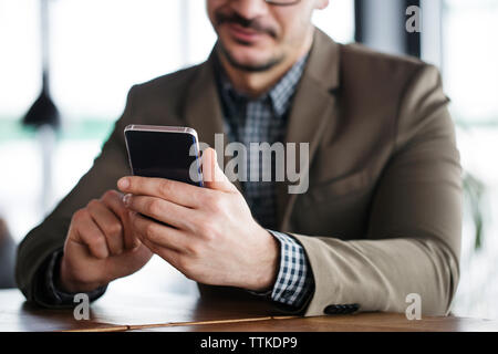 Midsection of smiling businessman using smart phone sitting in cafe Stock Photo