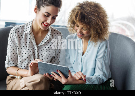 Happy female colleagues using tablet computer at cafe Stock Photo