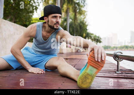 Man sitting and stretching on wooden walkway by river Stock Photo