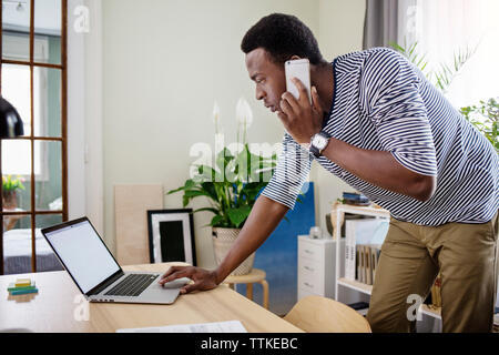 Side view of man using smart phone and laptop at home office Stock Photo