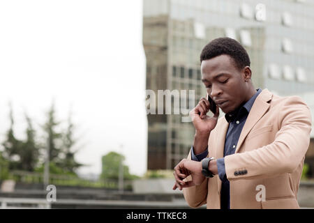 businessman checking the time while using smart phone in city Stock Photo