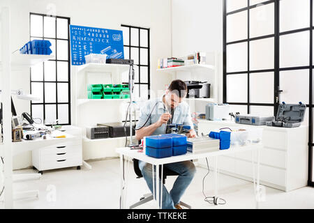 Engineer using drill on circuit board at table in electronic laboratory Stock Photo