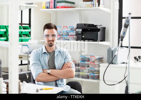 Portrait of smiling engineer wearing protective eyewear sitting at electronic laboratory Stock Photo