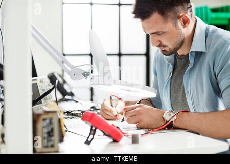 Concentrated engineer soldering circuit at table in electronics industry Stock Photo