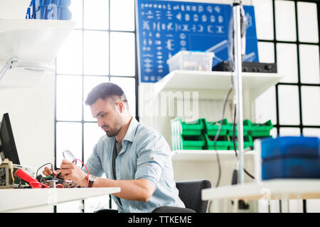 Serious engineer working on circuit board at table in electronics industry Stock Photo