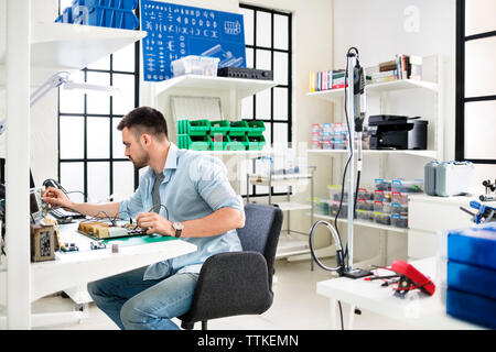Serious technician working on circuit board at table in electronics industry Stock Photo