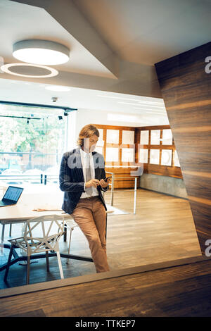 businessman leaning on desk while using smart phone in office Stock Photo