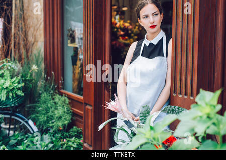 Thoughtful female florist standing at entrance of flower shop Stock Photo
