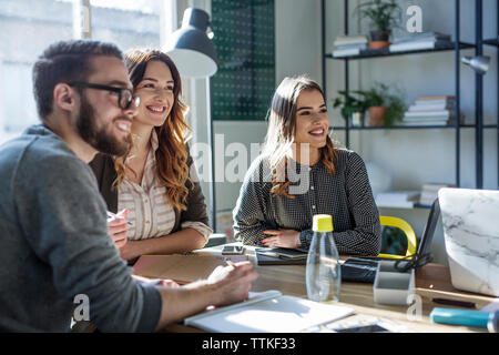 Smiling students looking away while sitting at table in classroom Stock Photo