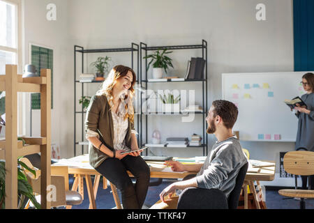 Smiling friends talking while sitting at desk in classroom Stock Photo