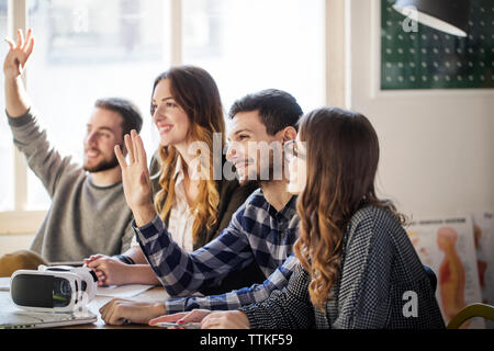 students raising hands while sitting in classroom Stock Photo