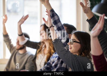 Students raising hands while sitting at table in classroom Stock Photo