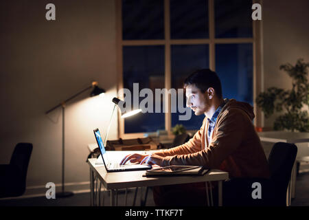 Side view of man studying through laptop computer in library at night Stock Photo