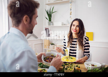 Happy woman eating spaghetti pasta while looking at friend in lunch party Stock Photo