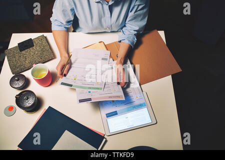 Midsection of businesswoman holding documents while sitting at desk in home office Stock Photo