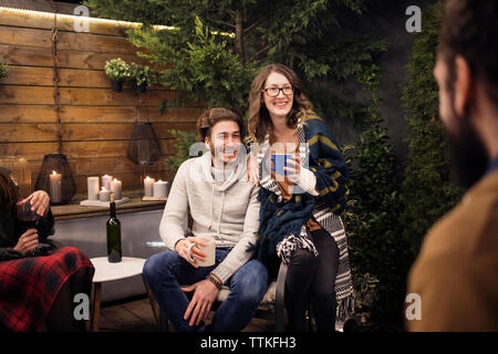 Happy friends talking while sitting in backyard at night Stock Photo