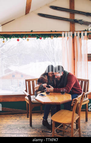 Couple using mobile phone while sitting by window in cafe Stock Photo