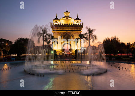 Patuxai Victory Monument (Vientiane Arc de Triomphe) and fountain floodlit at dusk, Vientiane, Laos, Southeast Asia Stock Photo