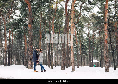 Happy couple looking at each other while standing on snowy field in forest Stock Photo