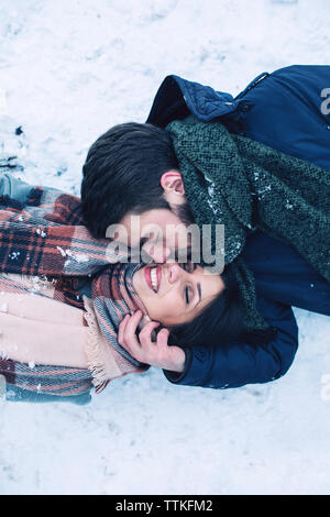 High angle view of man kissing girlfriend while lying on snow covered field Stock Photo