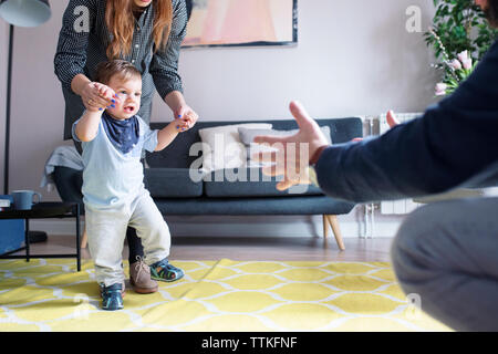 Mother assisting son in walking towards father at home Stock Photo