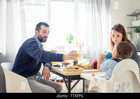 Man offering juice to son while having breakfast at table Stock Photo