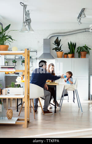 Mother looking at father assisting son in drinking water at table Stock Photo