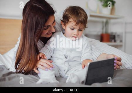Happy mother using tablet computer with baby boy on bed Stock Photo