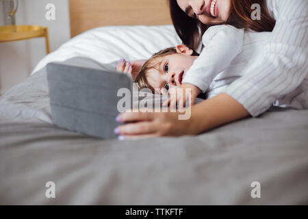 Baby boy using tablet computer with mother while lying in bed Stock Photo