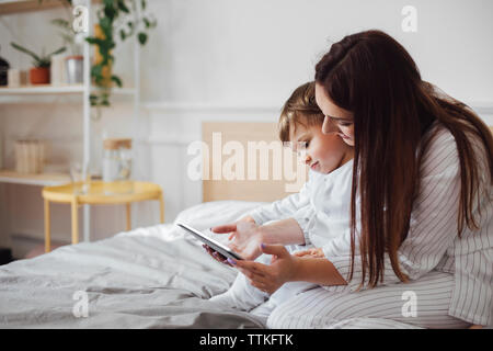 Mother and baby boy using tablet computer while sitting on bed Stock Photo