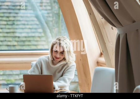 Woman using laptop computer while sitting by window at home Stock Photo