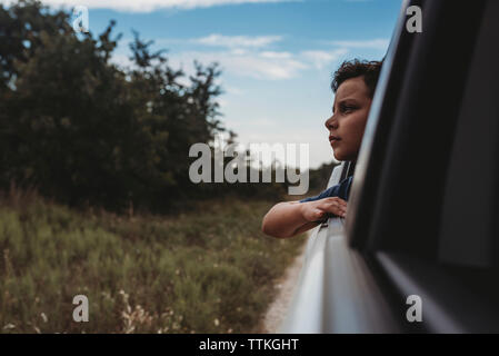 Thoughtful teenage boy looking through window in car