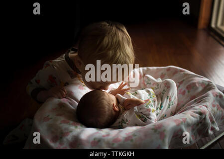 Brother kissing sister on forehead sleeping in moses basket at home Stock Photo