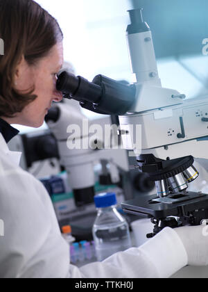 Professional female scientist in protective eyeglasses researching tube ...