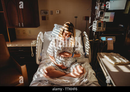 Pregnant woman touching stomach while sitting on bed in hospital Stock Photo