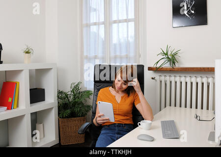 businesswoman using tablet computer while sitting on chair at home office Stock Photo