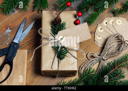 High angle view of Christmas present with labels and strings by pine needles on wooden table Stock Photo