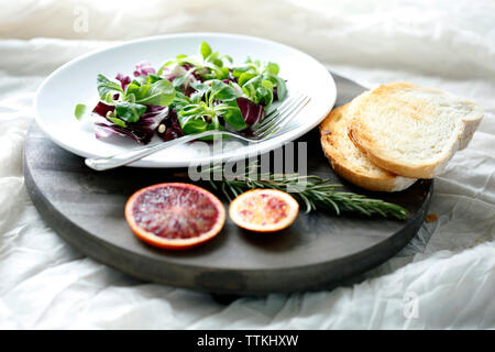 High angle view of salad with blood orange and rosemary by bread on cutting board
