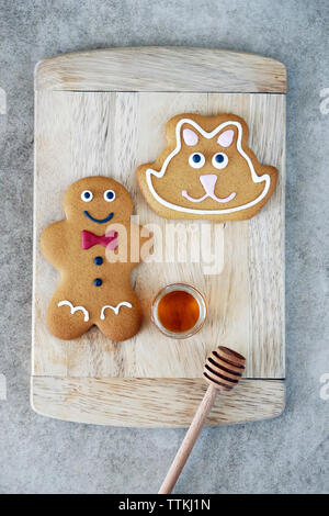 Overhead view of decorated gingerbread cookies with honey on wooden cutting board at table Stock Photo