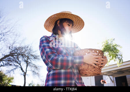 Young female farmer carrying basket in farm during sunny day Stock Photo