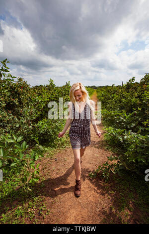 Happy female farmer walking on field against cloudy sky Stock Photo