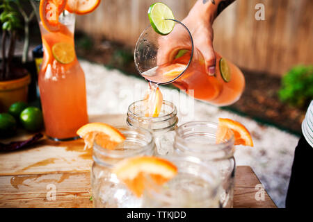 Cropped image of man pouring drink in glass jar on table Stock Photo
