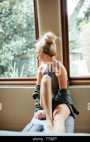 Woman looking away while sitting on seat by window at home Stock Photo